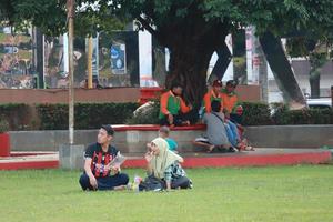 Kudus, December 2022. Photograph of visitors sitting relaxed enjoying the afternoon on the grass of the Kudus city square. photo