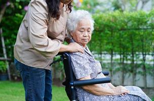 Caregiver help Asian elderly woman disability patient sitting on wheelchair in park, medical concept. photo