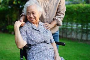 Caregiver help Asian elderly woman disability patient sitting on wheelchair in park, medical concept. photo