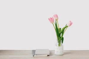 A bouquet of pink tulips of spring flowers in a vase stands on the desktop near the notebooks. Copy space photo