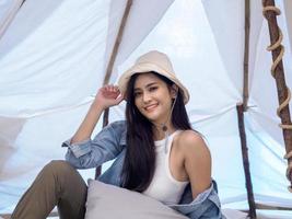 Portrait beautiful young girl woman Asian pretty smile one person alone sitting on chair camping with teble flower in vase lantern red travel trip in front tent freedom relax happy enjoy in vacation photo