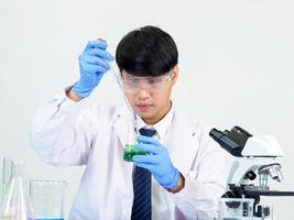 estudiante científico asiático en un laboratorio de mezcla de reactivos en un laboratorio de investigación científica con tubos de ensayo de varios tamaños y microscopios. sobre la mesa en el fondo blanco de laboratorio de química de laboratorio. foto