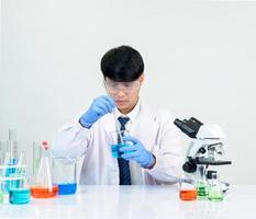 estudiante científico asiático en un laboratorio de mezcla de reactivos en un laboratorio de investigación científica con tubos de ensayo de varios tamaños y microscopios. sobre la mesa en el fondo blanco de laboratorio de química de laboratorio. foto