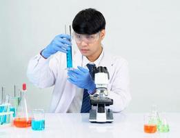 estudiante científico asiático en un laboratorio de mezcla de reactivos en un laboratorio de investigación científica con tubos de ensayo de varios tamaños y microscopios. sobre la mesa en el fondo blanco de laboratorio de química de laboratorio. foto