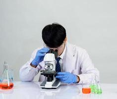 estudiante científico asiático en un laboratorio de mezcla de reactivos en un laboratorio de investigación científica con tubos de ensayo de varios tamaños y microscopios. sobre la mesa en el fondo blanco de laboratorio de química de laboratorio. foto