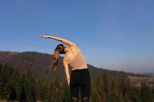 Young athletic woman stretching before intense morning workout at sunset or sunrise in beautiful mountain location. The concept of energy, health and harmony during sports photo