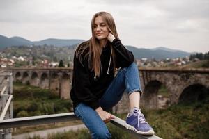 Young woman is sitting near old viaduct. Tourist girl in scenery countryside by the Historical abandoned railway arch bridge viaduct in Vorokhta, Ivano-Frankivsk Region, Ukraine photo