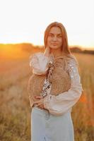 beautiful young woman with long hair and straw bag in hand in the summer at sunset in the field for a walk. she is happy. background blurred art photography. summer holiday concept. photo