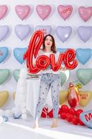 Love. A happy bright girl in the shape of hearts holds in her hands an inflatable ball the word Love on many colorful heart balloons background. smiles,funny Valentine s Day birthday party. photo