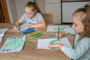 Children draw the planet Earth with pencils and felt-tip pens on album sheets for Earth Day at their home table. The concept of protecting the environment, peace on Earth. photo