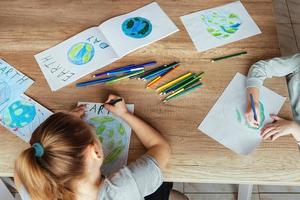 niños dibujar el planeta tierra con lapices y punta de fieltro plumas en álbum hojas para tierra día a su hogar mesa. el concepto de proteger el ambiente, paz en tierra. foto