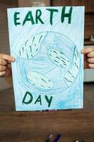 The child holds a drawing of the planet Earth with a map of the world, painted with multi-colored pencils and felt-tip pens on white paper. Peace and earth day concept, environmental protection. photo