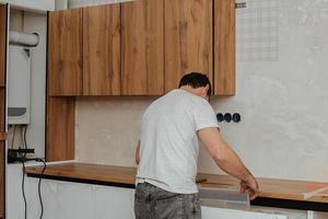 Craftsman, furniture maker and assembler, installs a modern kitchen in the house with tools in hand. Custom furniture concept, home improvement, renovation photo