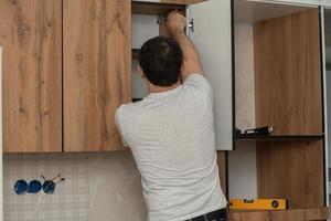 Craftsman, furniture maker and assembler, installs a modern kitchen in the house with tools in hand. Custom furniture concept, home improvement, renovation photo