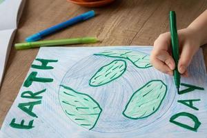 A child at home at the table draws the planet Earth with a world map with multi-colored pencils and felt-tip pens on white paper. Peace and earth day concept. photo