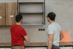 Two craftsmen, furniture makers and assemblers, are installing a modern kitchen in a home, tools in their hands. Concept furniture to order, improvement of living conditions, repair photo