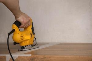 The furniture master installs a modern kitchen in the house, in his hands is an electric jigsaw with which he cuts a place for a sink in the countertop. photo