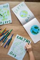 A child at school at the table draws the planet Earth with a world map with multi-colored pencils and felt-tip pens on white paper. Peace and earth day concept. photo