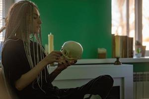 A young bright girl in dark clothes, with dreadlocks on her head, holds a skull in her hands. Generation z, gothic style photo