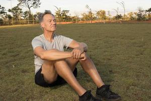 Mature Man sitting on the grass relaxing after working out in the park photo