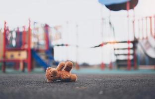 Lost teddy bear toy lying don on playground floor in gloomy day,Lonely and sad brown bear doll lied down alone in the park,lost toy or Loneliness concept,International missing Children day photo