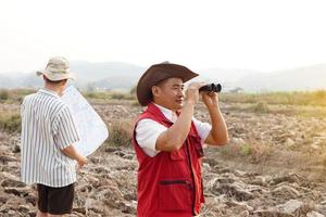 Asian father and son are exploring and surveying their own land, father holds binocular and points to boundary, son holds map. Concept, land property, legacy.Exploration. photo