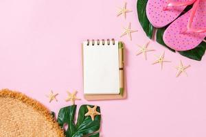 Beach accessories with straw hat, sunscreen bottle and seastar on pink background top view with copy space photo