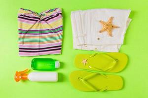 Flat lay composition with green Beach accessories on green color background. Summer holiday background. Vacation and travel items top view photo