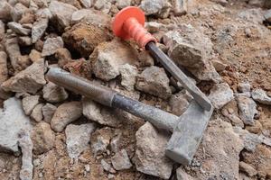 selective focus to stone chisel and hammer on collapsed building rubble, demolished building renovation and evacuation concept, soft focus photo