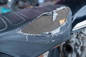 selectivo fokus en el lacerado motocicleta asiento , antiguo negro cuero asiento es dañar , roto cuero. foto