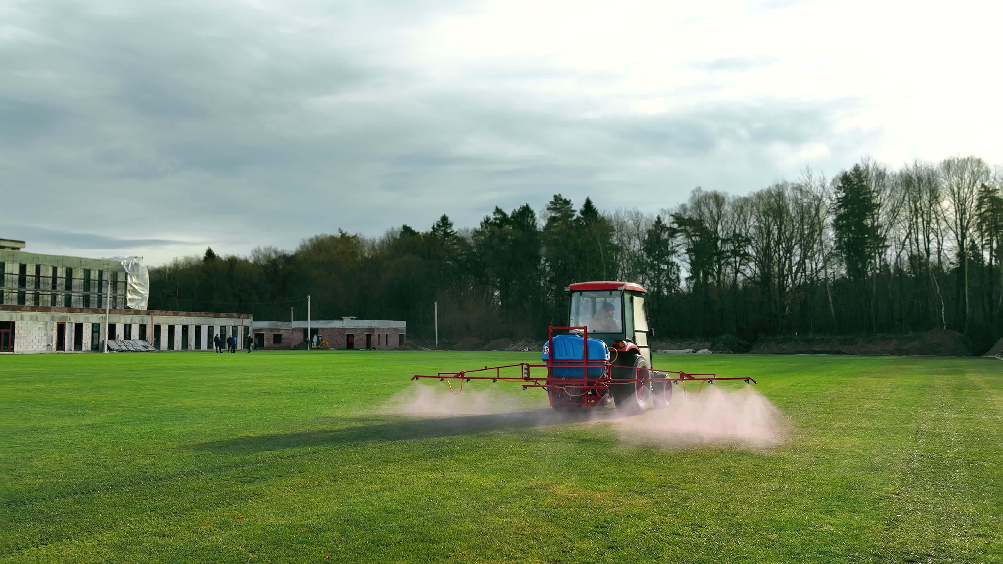 The tractor sprinkles the grass of the football field. Maintenance of