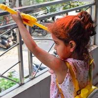 Sweet little Indian girl playing colours on Holi festival, holding pichakaree full of colours, Holi festival celebrations in Delhi, India photo