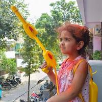 Sweet little Indian girl playing colours on Holi festival, holding pichakaree full of colours, Holi festival celebrations in Delhi, India photo