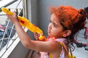 Sweet little Indian girl playing colours on Holi festival, holding pichakaree full of colours, Holi festival celebrations in Delhi, India photo