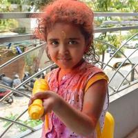 Sweet little Indian girl playing colours on Holi festival, holding pichakaree full of colours, Holi festival celebrations in Delhi, India photo