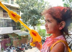 Sweet little Indian girl playing colours on Holi festival, holding pichakaree full of colours, Holi festival celebrations in Delhi, India photo