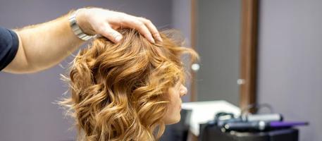 Hairdresser checks curly hairstyle of woman photo