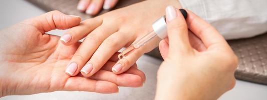 Hand of manicurist pours oil to cuticle photo