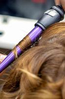 Hairdresser makes hairstyle by curling iron photo