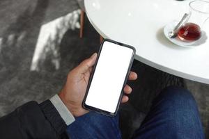 mano de hombre joven usando un teléfono inteligente con pantalla verde en el café foto