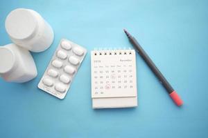 medical pill container and calendar on color background photo