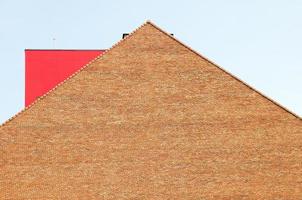 Red brick building top with a red metal object on the roof. photo