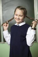 Funny schoolgirl with pigtails, middle school age on the background of the blackboard. photo