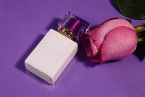 White perfume bottle with purple top and rose with water drops. mockup photo