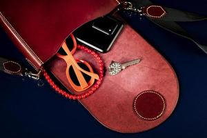 Red leather bag with women's accessories on a dark background. photo