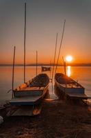 dos pequeño barcos amarrado en el apuntalar de el lago. a puesta de sol foto