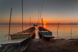 dos pequeño barcos amarrado en el apuntalar de el lago. a puesta de sol foto