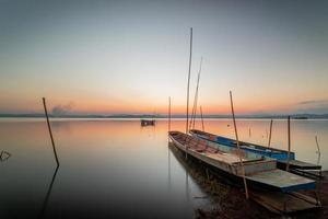 dos pequeño barcos amarrado en el apuntalar de el lago. a puesta de sol hermosa ligero foto