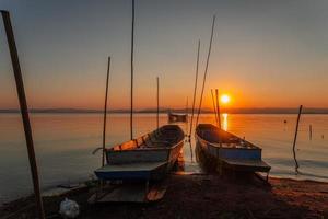 dos pequeño barcos amarrado en el apuntalar de el lago. a puesta de sol foto