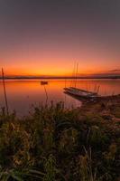 dos pequeño barcos amarrado en el apuntalar de el lago. a puesta de sol hermosa ligero foto